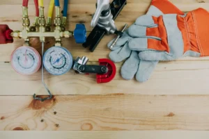 Cranney Home Services HVAC tools and gloves neatly displayed on wood, featuring pressure gauges, pipe cutter, and safety gear.
