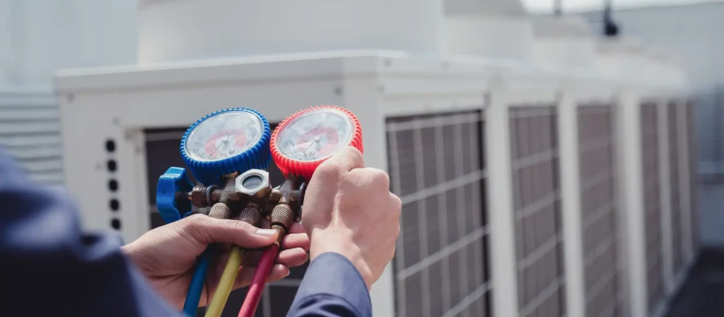 A Cranney Home Services technician checks HVAC system pressure on a rooftop, using a manifold gauge set near multiple AC units.