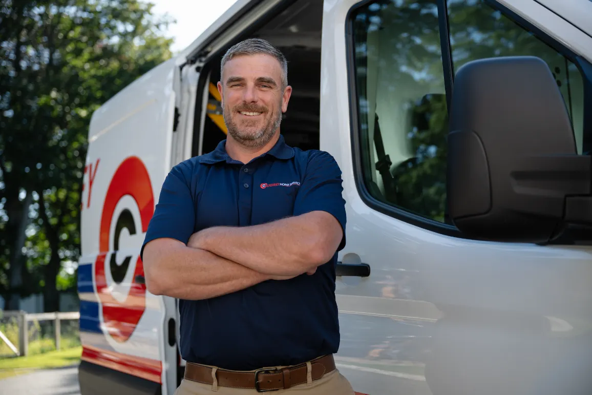 A Cranney Home Services team member in a navy polo stands confidently before a branded service van on a bright, sunny day.