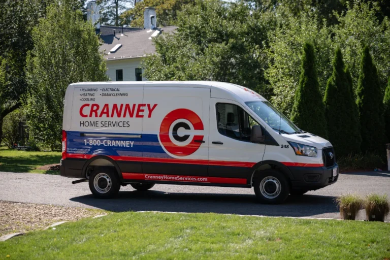 A white Cranney Home Services van with company branding and contact information is parked on a driveway near a house and trees.