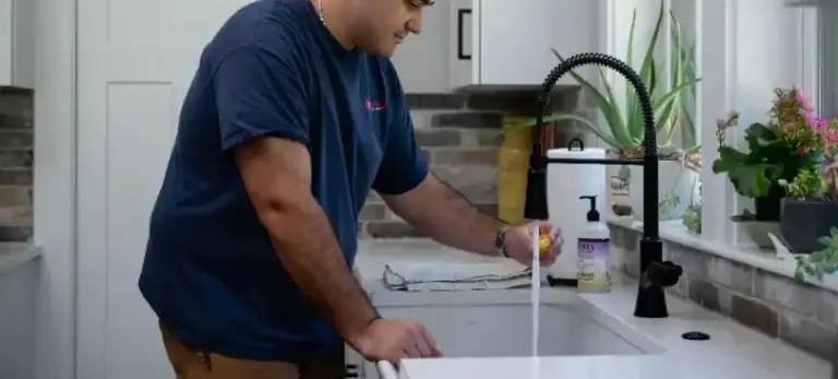 A Cranney Home Services technician rinses a cup at a kitchen sink, with plants and cleaning supplies neatly arranged on the counter.