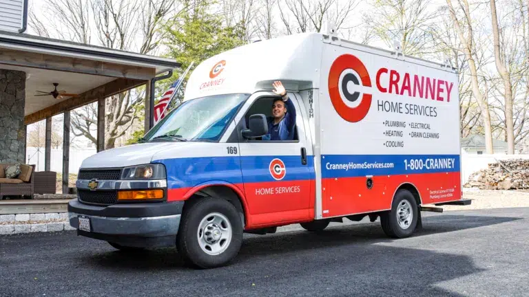 A Cranney Home Services van is parked in a Boxford driveway. A person sits in the driver's seat, smiling and waving out the window. The van displays company branding and contact information.