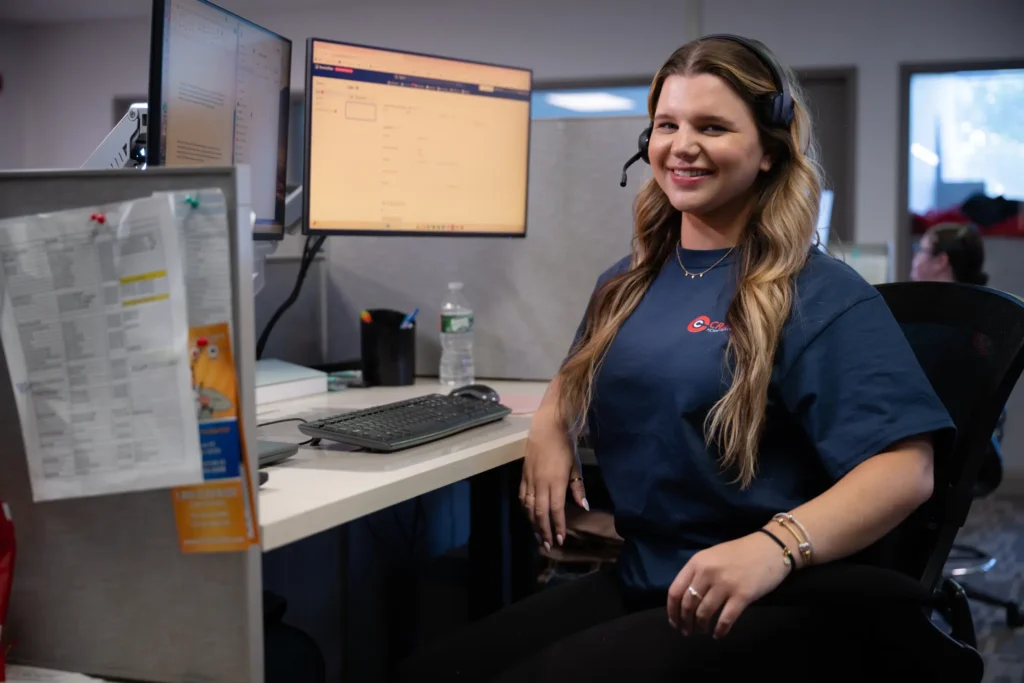%Focuskw% | Cranney Home Services A woman wearing a headset sits at an office desk with dual monitors, a desktop computer, documents pinned to a divider, and a water bottle nearby.