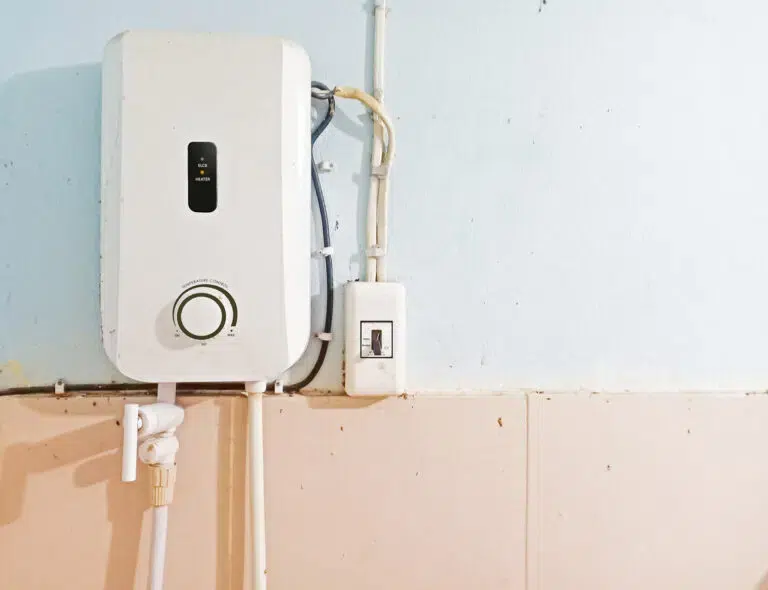 A Danvers wall-mounted water heater with control dial and switches is installed above beige tiles and against a light blue wall.